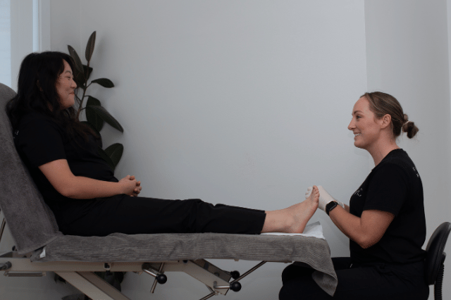 Female patient sitting on treatment bed with female podiatrist discussing diabetic foot care