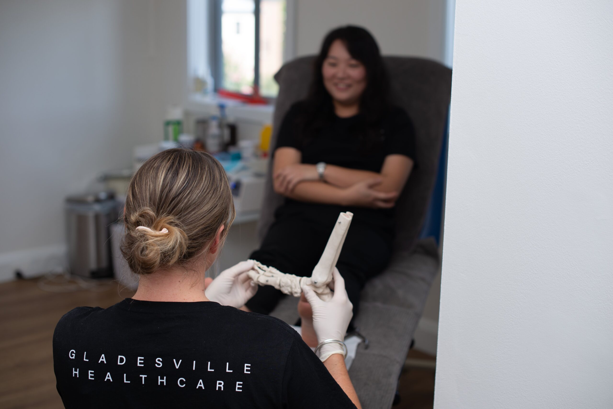 A healthcare worker shows a foot model to a seated patient in a clinic room.