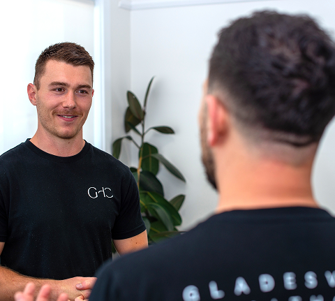 Two men are having a conversation indoors near a potted plant.