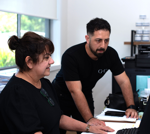 Two people in an office, one seated at a computer and the other standing beside her.