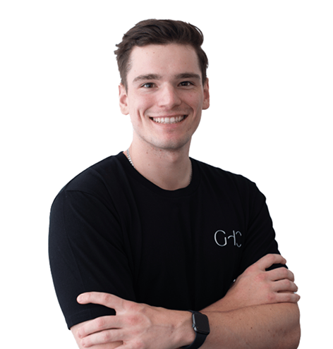 Young man with short brown hair smiling, wearing a black t-shirt and smartwatch, arms crossed.