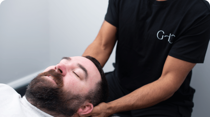 A man receives a neck massage from a person wearing a black shirt.