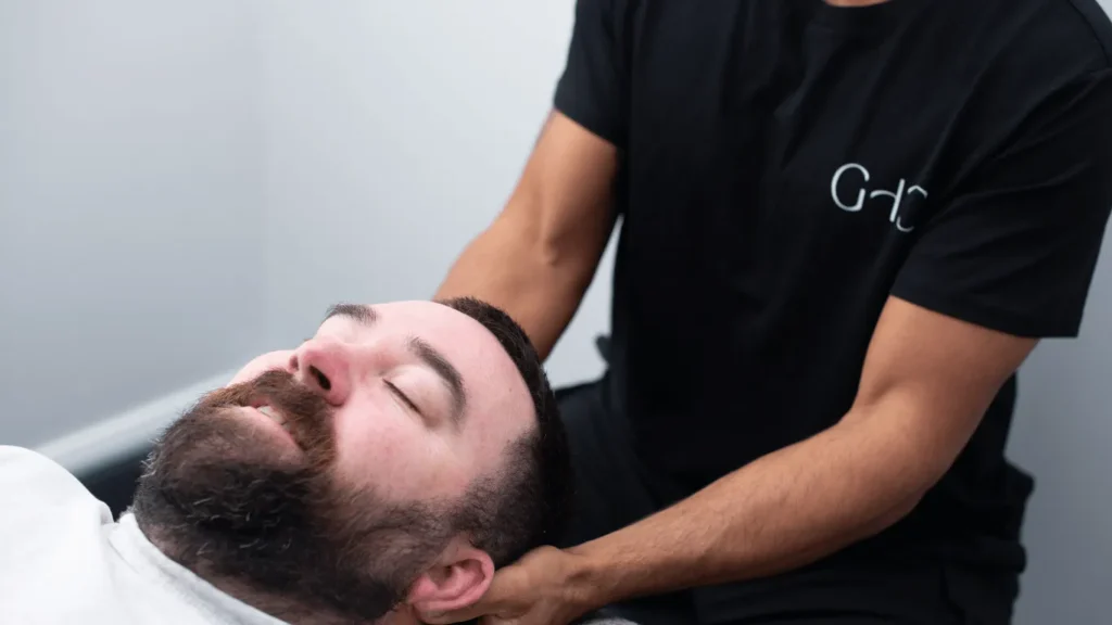 A man receives a neck massage from another person wearing a black shirt.