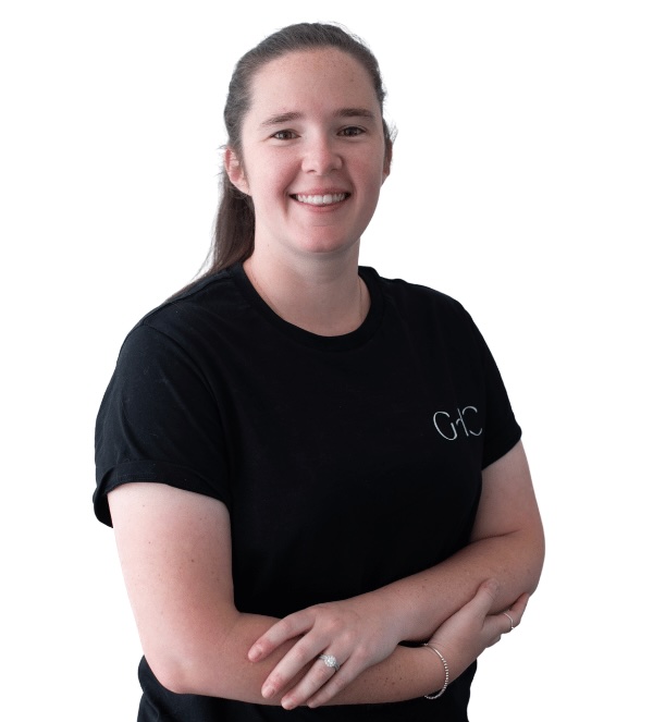 Woman with long brown hair in a black t-shirt, smiling with arms crossed against white background.
