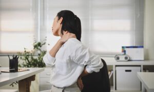 Person at desk holding neck and back, showing pain—possibly seeking plantar fasciitis treatment.