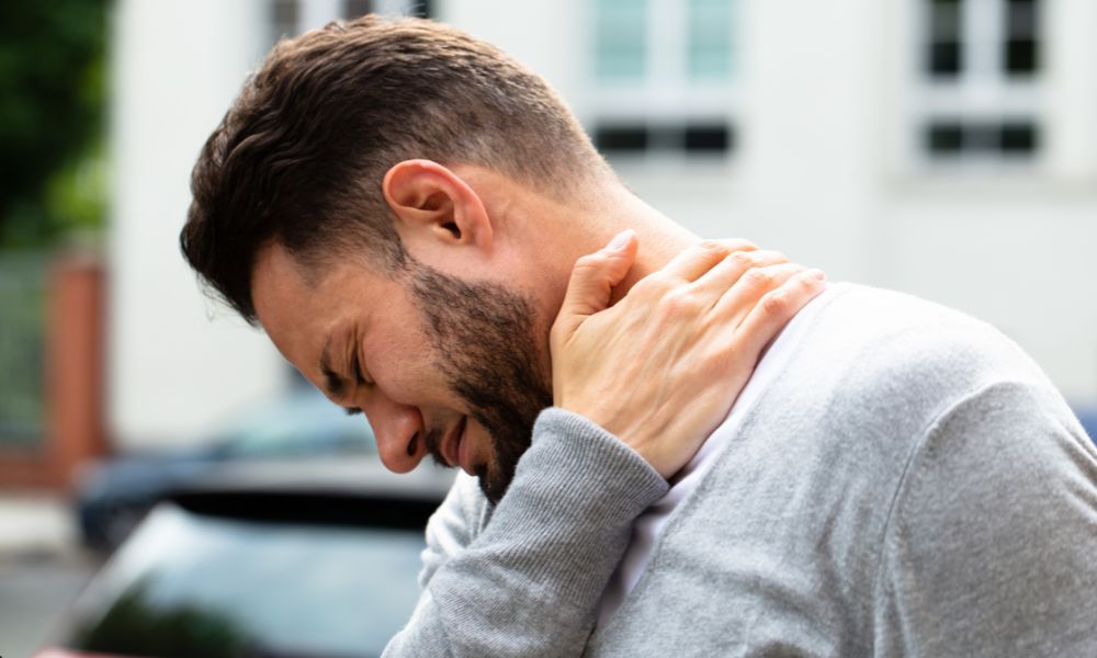 Man outdoors holding his neck, suggesting discomfort while recovering from a sports injury.