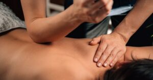 A person receives a Deep Tissue vs Remedial Massage on their bare upper back from a therapist.