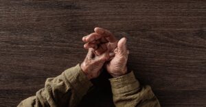 Elderly hands in a green shirt resting together, managing Parkinson’s Disease with care.